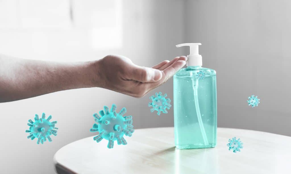 Image of a hand reaching for a hand sanitiser bottle with virus particles floating around it.